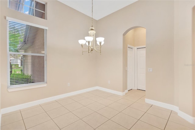 empty room with lofted ceiling, an inviting chandelier, and light tile patterned floors