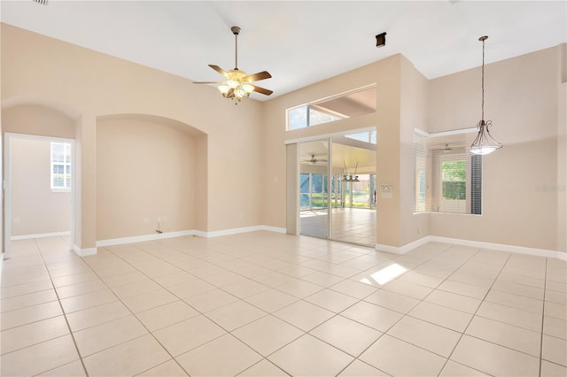 tiled empty room featuring ceiling fan, a towering ceiling, and a wealth of natural light