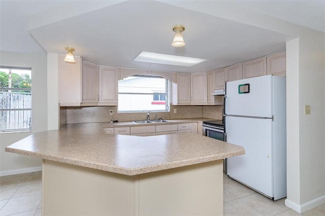 kitchen with tasteful backsplash, light countertops, freestanding refrigerator, a sink, and a peninsula