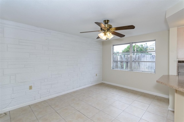 empty room featuring baseboards, ceiling fan, brick wall, and light tile patterned floors