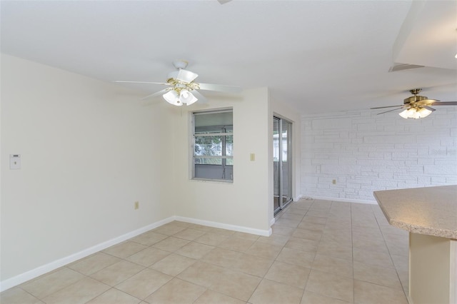 spare room featuring a ceiling fan, baseboards, brick wall, and light tile patterned floors