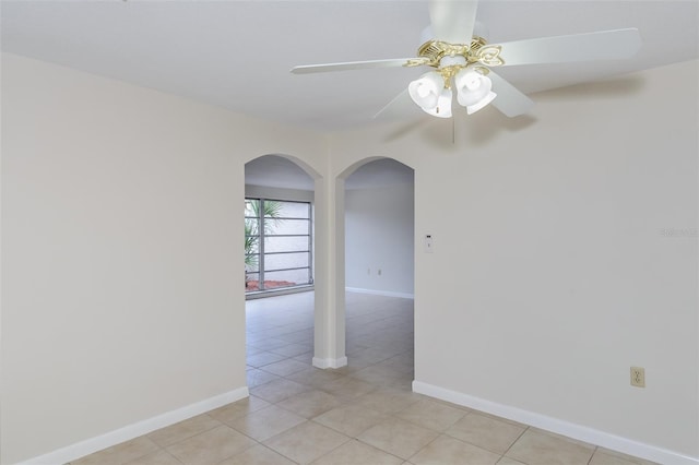 unfurnished room featuring light tile patterned flooring, baseboards, arched walkways, and ceiling fan