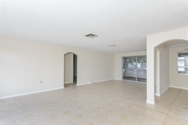 empty room featuring arched walkways, visible vents, and baseboards