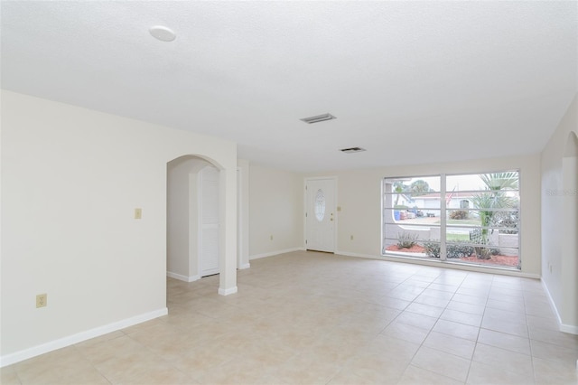 unfurnished room featuring light tile patterned floors, visible vents, arched walkways, and baseboards