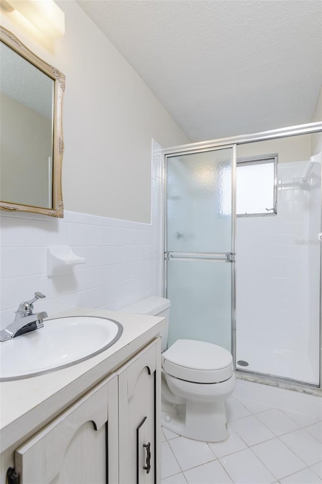 bathroom with a textured ceiling, tile patterned flooring, toilet, tile walls, and a stall shower