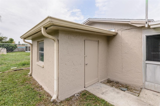 property entrance with a lawn, fence, and stucco siding