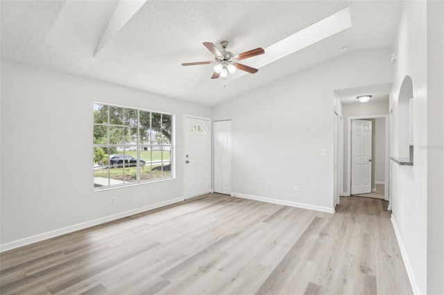 empty room featuring light hardwood / wood-style floors, a textured ceiling, ceiling fan, and vaulted ceiling with skylight