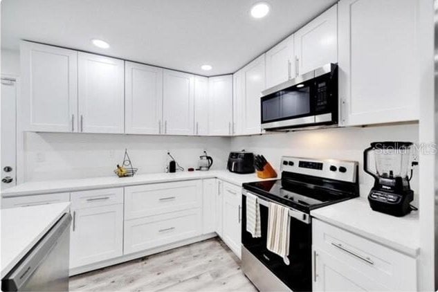 kitchen with light hardwood / wood-style floors, stainless steel appliances, and white cabinets