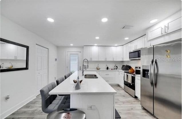 kitchen featuring sink, a kitchen bar, stainless steel appliances, white cabinets, and a center island with sink