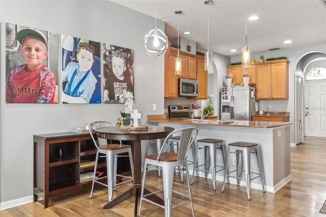 kitchen featuring light hardwood / wood-style floors, stainless steel appliances, kitchen peninsula, and hanging light fixtures