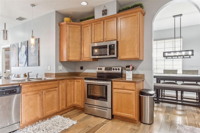 kitchen with stainless steel appliances, dark stone countertops, sink, decorative light fixtures, and light hardwood / wood-style floors