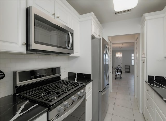 kitchen with white cabinets, appliances with stainless steel finishes, light tile patterned floors, and a notable chandelier