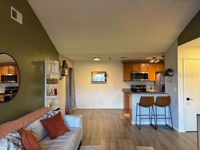 kitchen with ceiling fan, appliances with stainless steel finishes, a breakfast bar, vaulted ceiling, and light hardwood / wood-style flooring