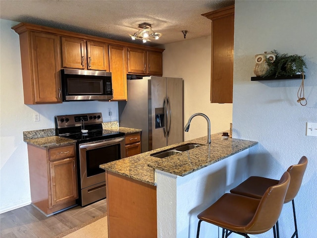 kitchen with light hardwood / wood-style flooring, kitchen peninsula, dark stone counters, sink, and appliances with stainless steel finishes