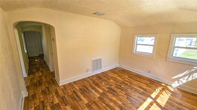 spare room with lofted ceiling, a textured ceiling, and dark wood-type flooring