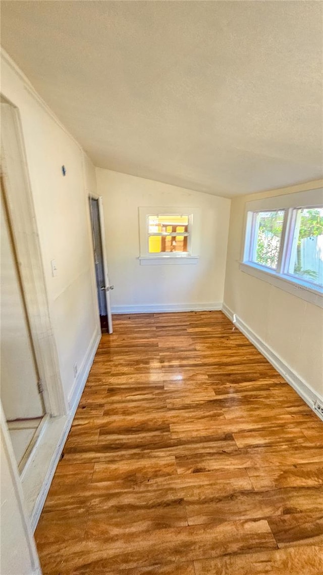 spare room featuring a textured ceiling, lofted ceiling, and light wood-type flooring