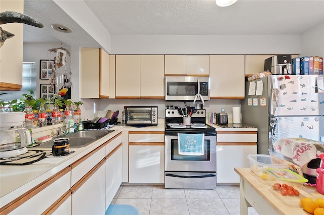 kitchen featuring sink, appliances with stainless steel finishes, a textured ceiling, light tile patterned flooring, and cream cabinetry