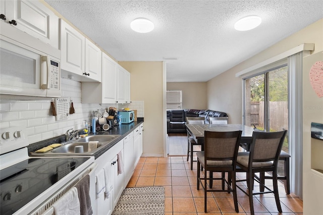 kitchen with white cabinetry, white appliances, light tile patterned flooring, and backsplash