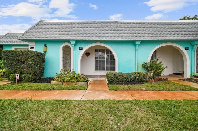 view of front facade with stucco siding, a front lawn, and a shingled roof