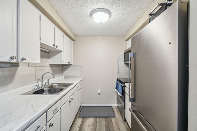 kitchen with appliances with stainless steel finishes, white cabinetry, a textured ceiling, light wood-type flooring, and sink