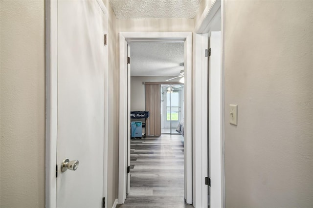 corridor with a textured ceiling and hardwood / wood-style flooring