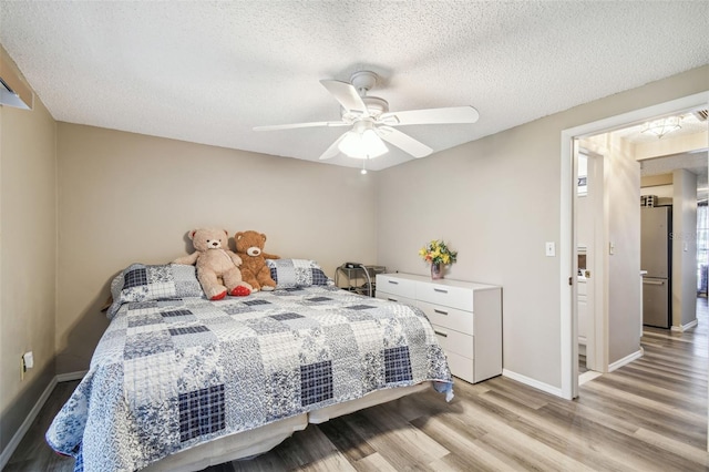 bedroom featuring ceiling fan, stainless steel refrigerator, a textured ceiling, and light hardwood / wood-style floors