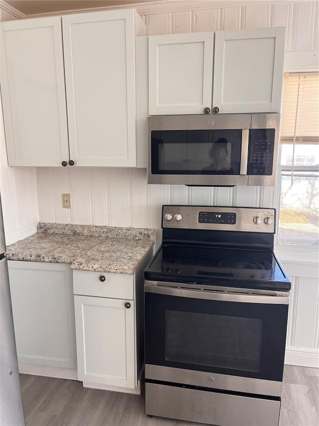 kitchen featuring light stone countertops, light hardwood / wood-style flooring, white cabinets, and stainless steel appliances