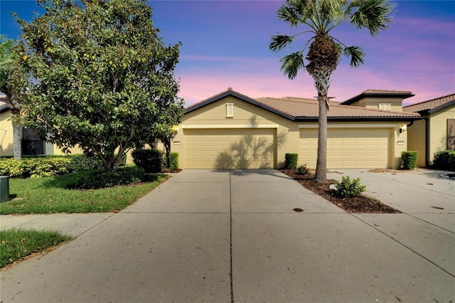 ranch-style house featuring a tile roof, stucco siding, a garage, and concrete driveway
