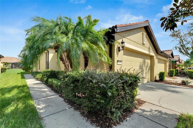 view of side of property featuring a tiled roof, a yard, a garage, concrete driveway, and stucco siding