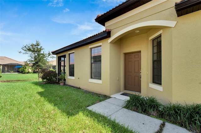 view of exterior entry with a yard, a tiled roof, and stucco siding