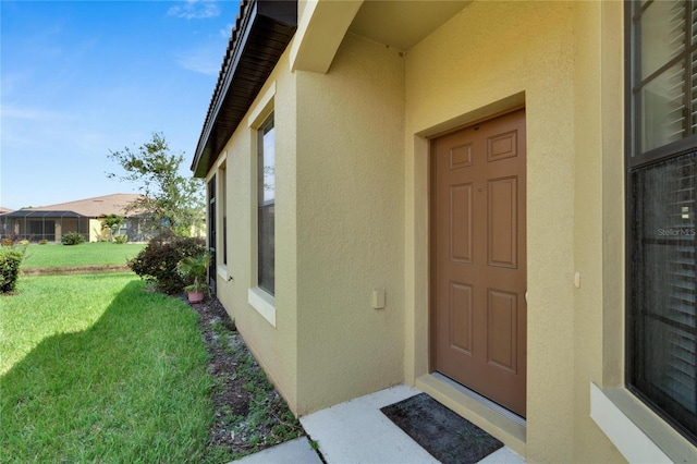 view of exterior entry with stucco siding and a lawn
