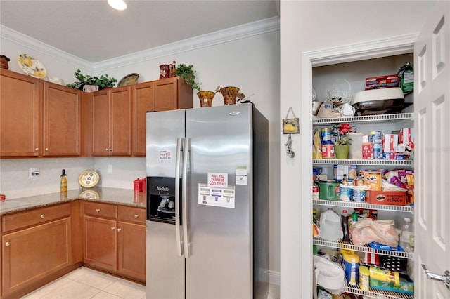 kitchen featuring light tile patterned floors, stainless steel fridge, ornamental molding, brown cabinets, and light stone countertops