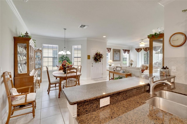 kitchen with stone counters, sink, hanging light fixtures, light tile patterned flooring, and ornamental molding