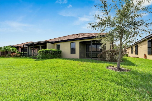 back of property featuring a yard, a tile roof, a sunroom, and stucco siding
