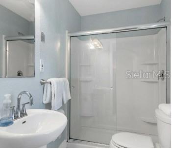 bathroom featuring sink, a shower with shower door, and toilet