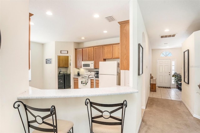 kitchen featuring separate washer and dryer, kitchen peninsula, white appliances, a kitchen bar, and light carpet