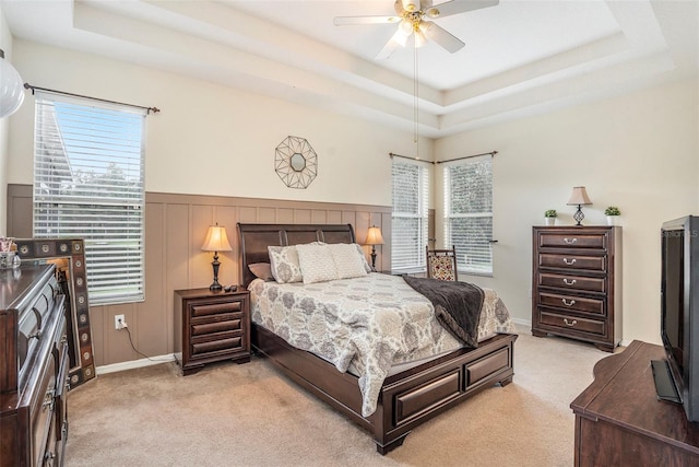 carpeted bedroom with ceiling fan, multiple windows, and a tray ceiling