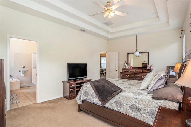 bedroom featuring ceiling fan, a raised ceiling, light colored carpet, and ensuite bathroom