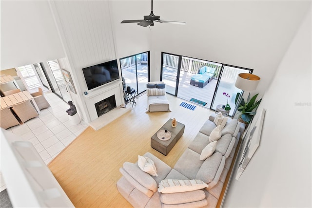 tiled living room with ceiling fan, a fireplace, and a high ceiling