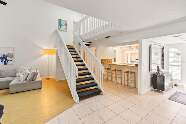 stairway with a textured ceiling, a ceiling fan, baseboards, visible vents, and tile patterned floors