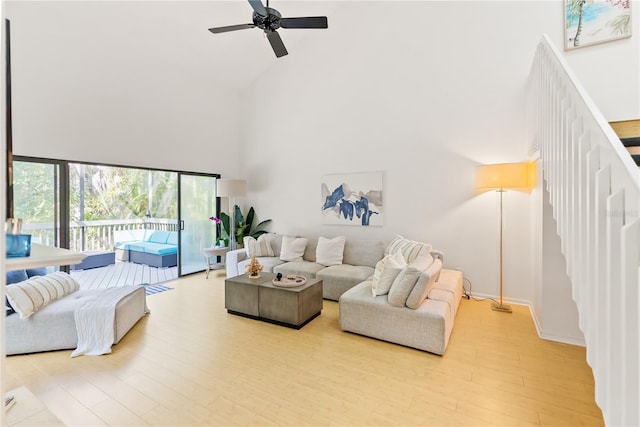 living area featuring light wood-style flooring, a high ceiling, stairway, and a ceiling fan