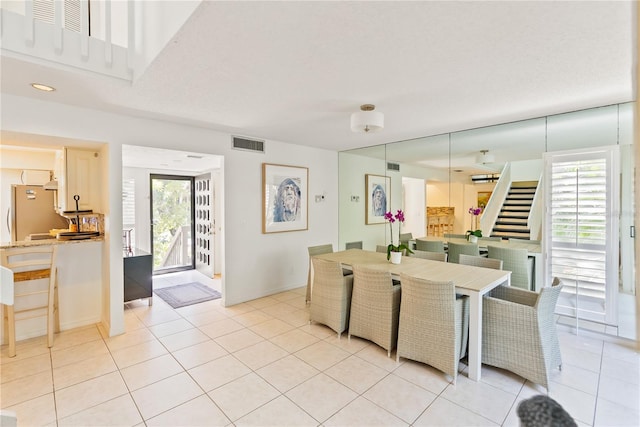 dining room featuring light tile patterned flooring, visible vents, baseboards, and stairs