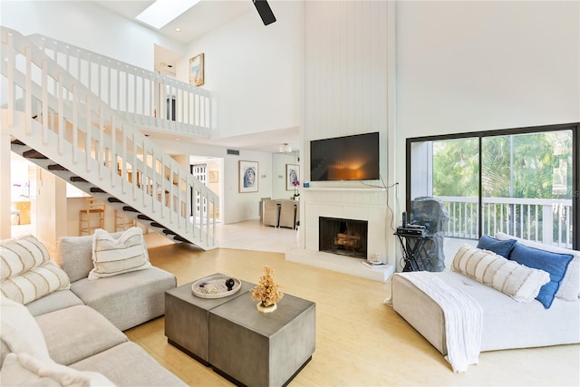 living room with a large fireplace, light wood-type flooring, a high ceiling, and a skylight