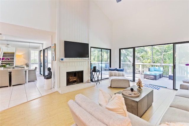 living room featuring a tiled fireplace, a towering ceiling, and light hardwood / wood-style floors