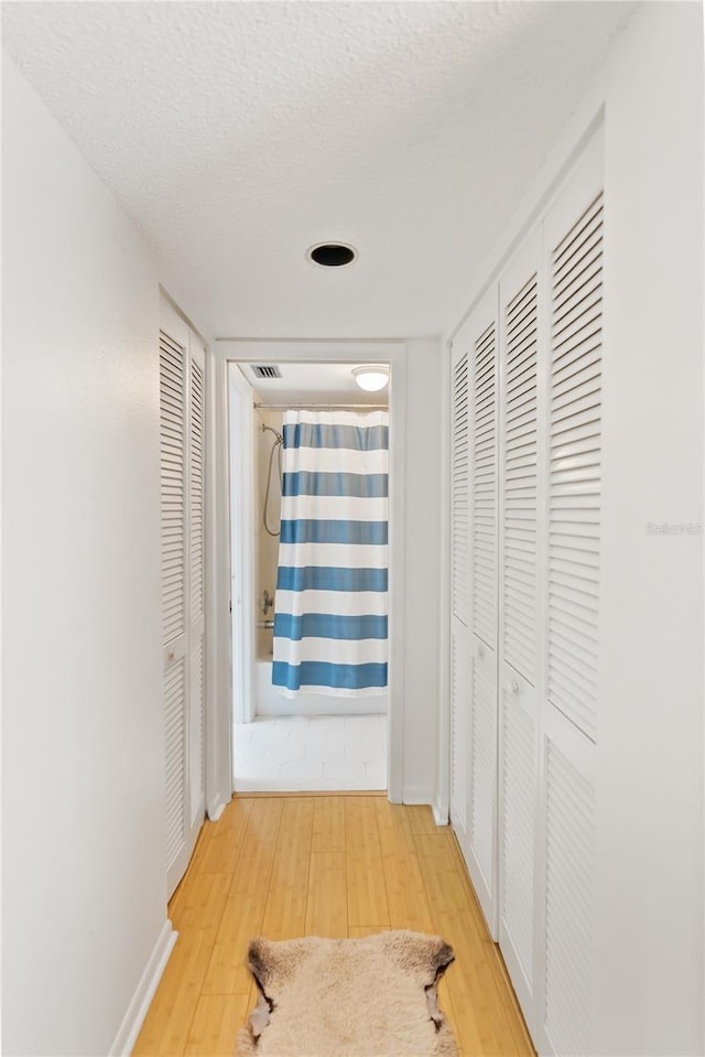 hall featuring a textured ceiling, wood finished floors, visible vents, and baseboards