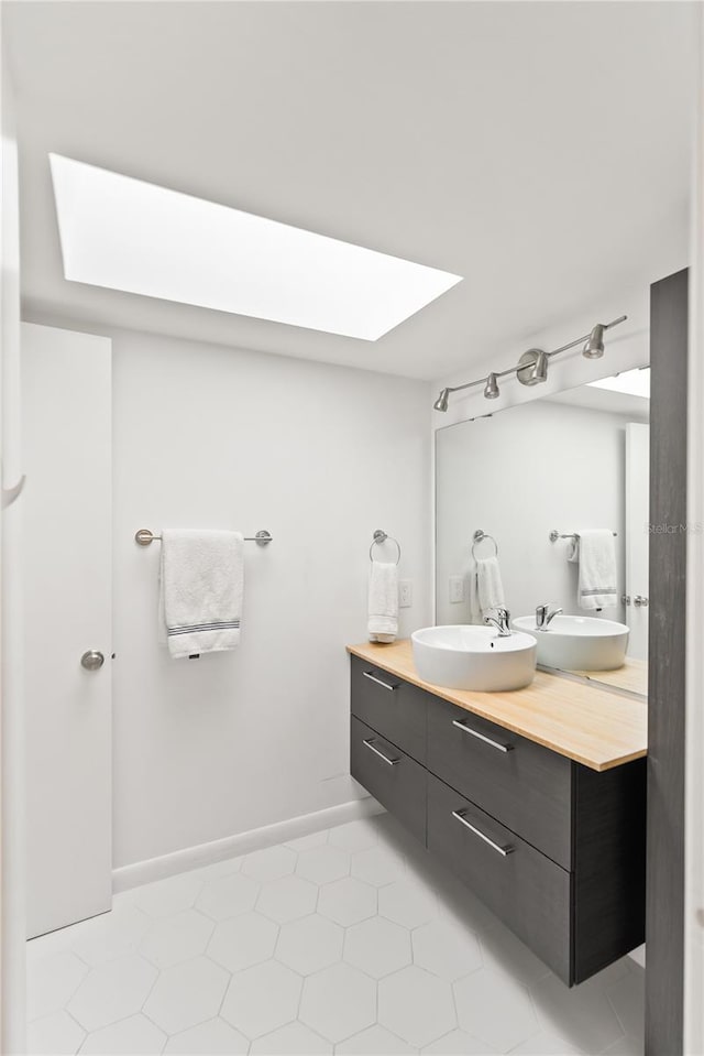 full bath with double vanity, a skylight, a sink, and baseboards