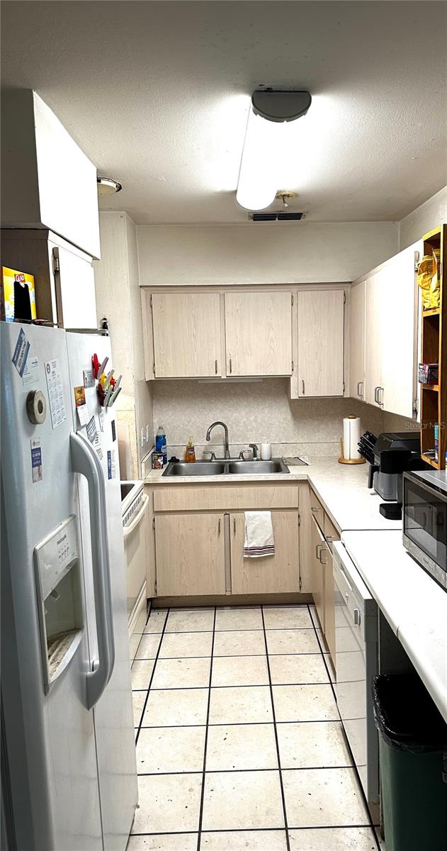 kitchen with light tile patterned floors, a textured ceiling, light brown cabinetry, sink, and white appliances