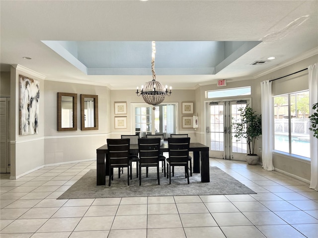 tiled dining room with french doors, a raised ceiling, ornamental molding, and a chandelier