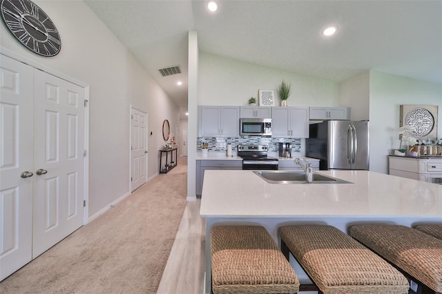 kitchen with appliances with stainless steel finishes, an island with sink, gray cabinets, a breakfast bar, and light colored carpet