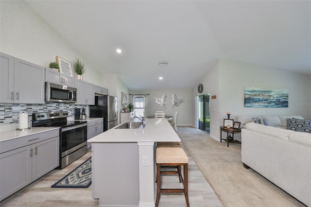 kitchen featuring lofted ceiling, a center island with sink, a kitchen breakfast bar, gray cabinets, and stainless steel appliances